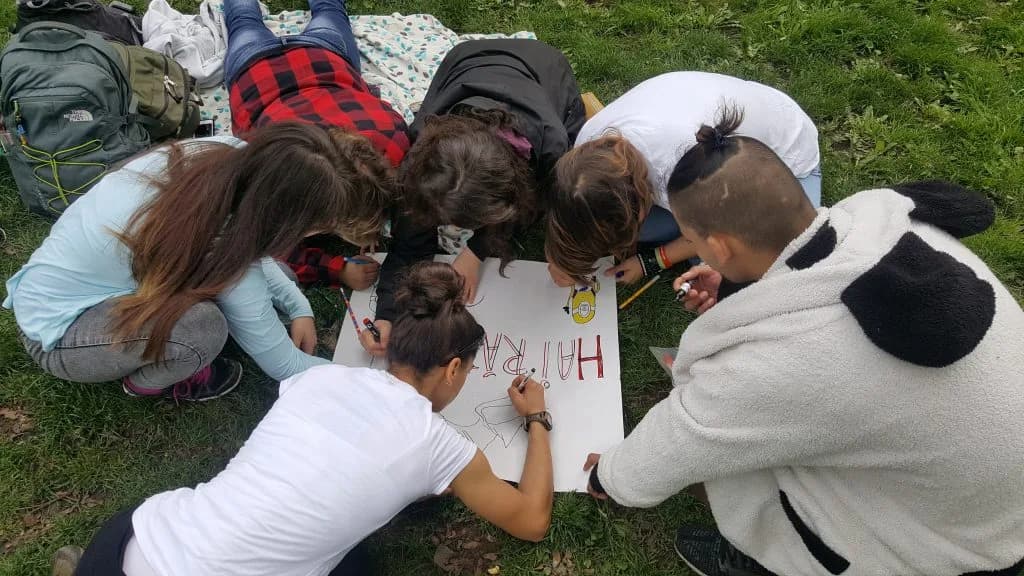 Copii și voluntari desenează împreună pe un carton așezat pe iarbă