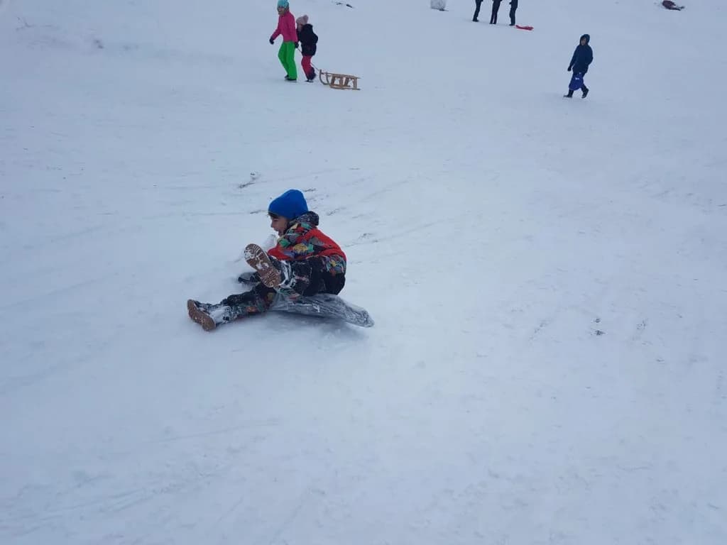 Un copil cu căciulă albastră stă pe sanie în zăpadă