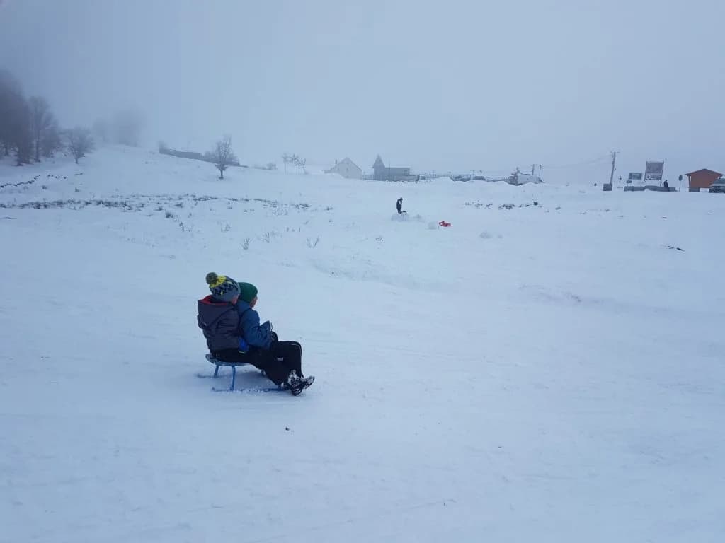 Doi participanți la săniuș se odihnesc pe sanie la baza dealului